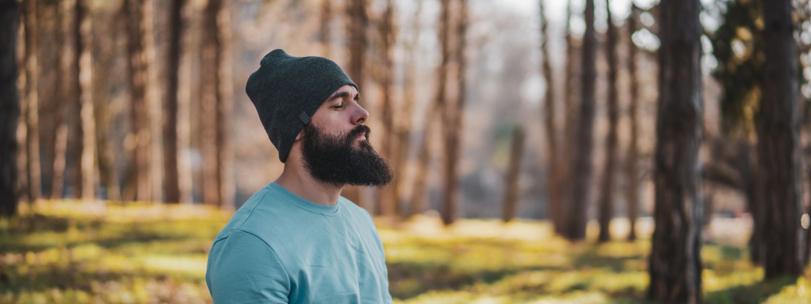 man wiith beard in a beanie meditating in the woods