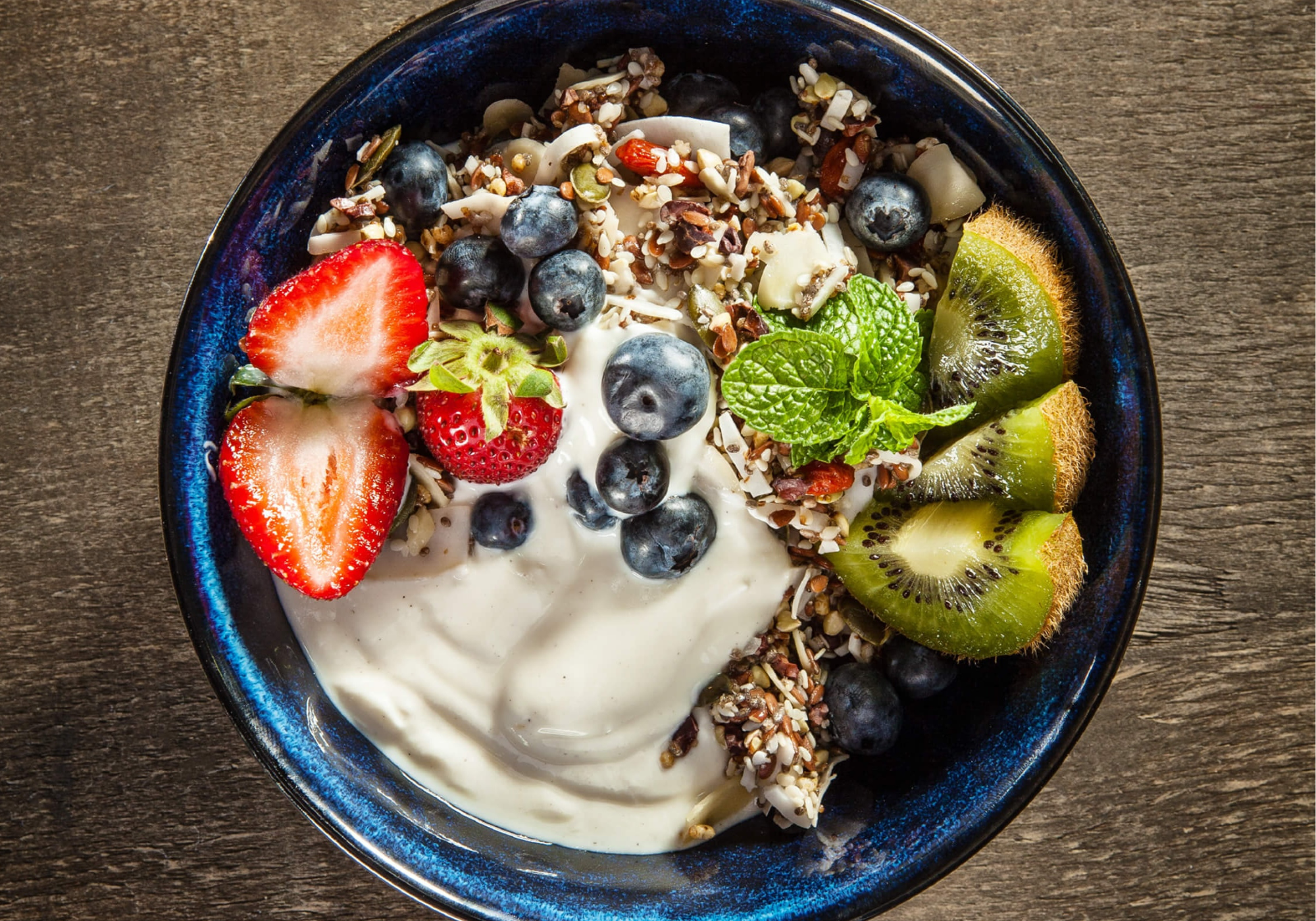 Yogurt bowl with goodMix Blend11 muesli, berries, and kiwi on a wooden surface.