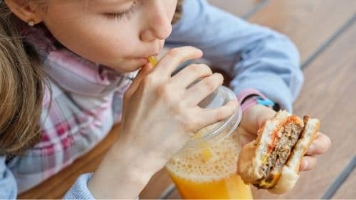 child eating burger and orange juice