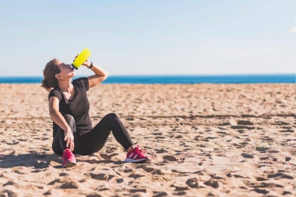 woman sitting on sand drinking water