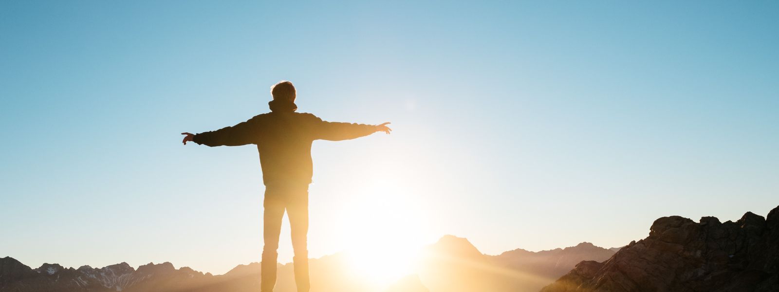 silhouette with arms outstretched as sun sets