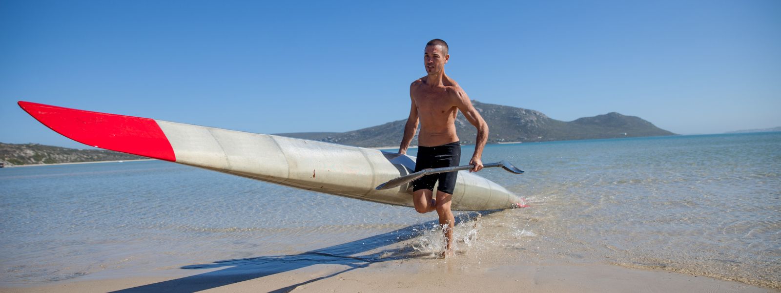 athlete running from the water with a surf ski