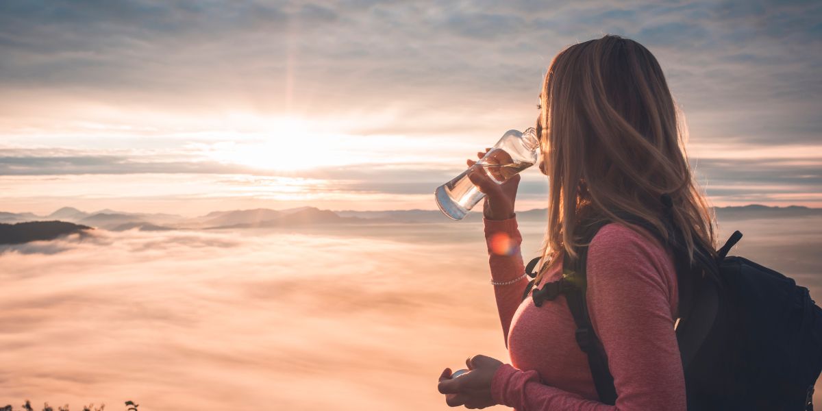 how to slow down ageing: woman drinking water observing a sunset above clouds