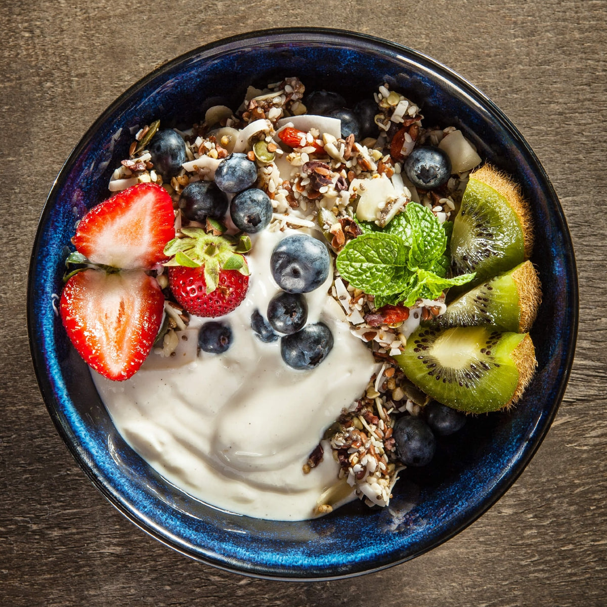 Yogurt bowl with goodMix Blend11 muesli, berries, and kiwi on a wooden surface.